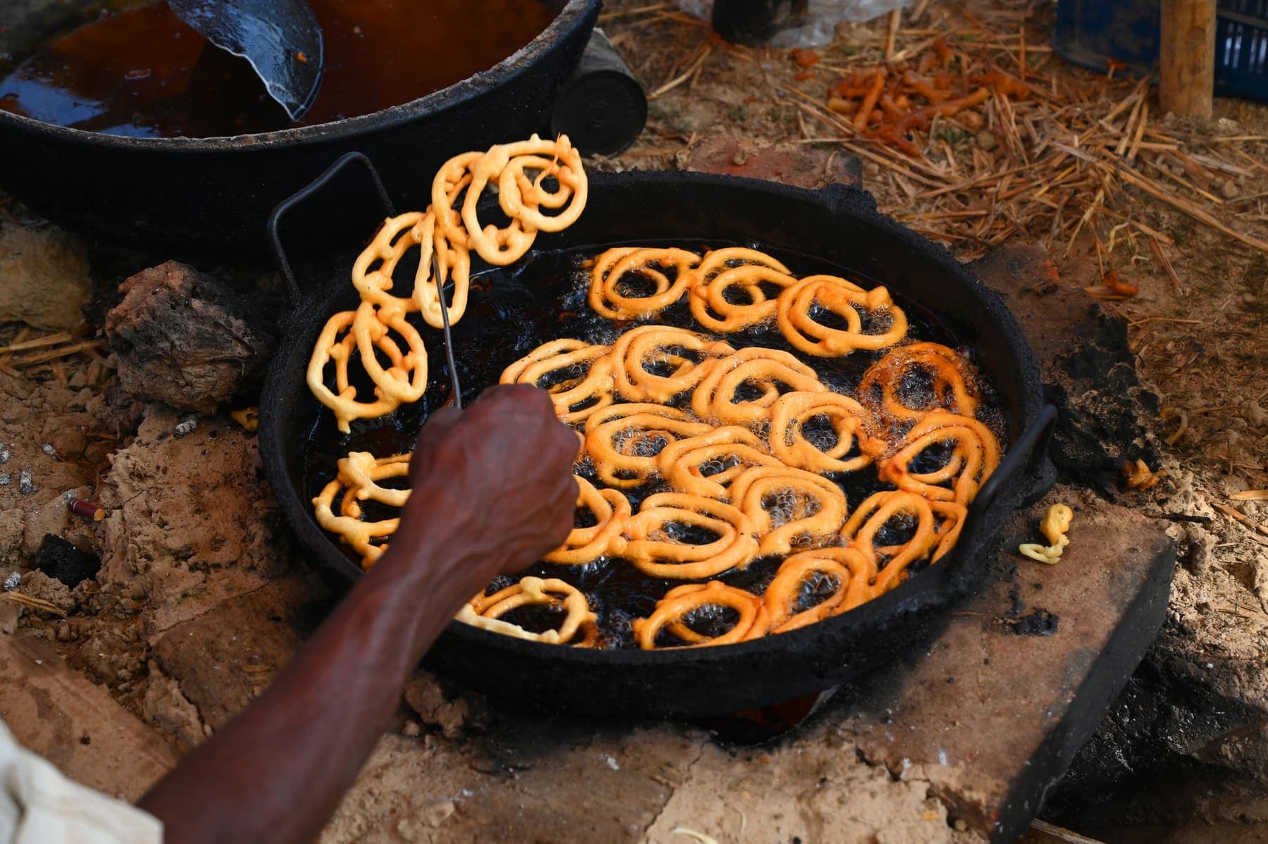 Jalebi coils frying in a wide iron pan of oil